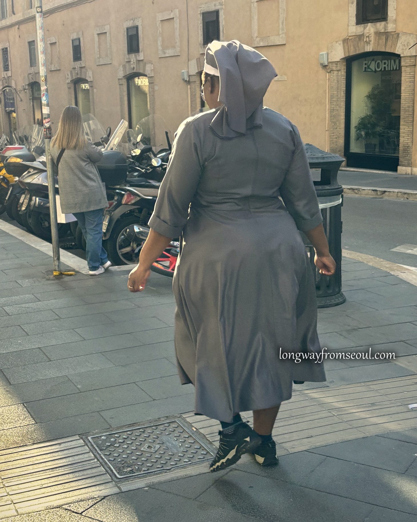 A nun in a grey habit walking a Rome street in morning light