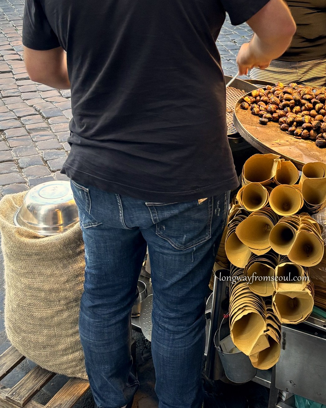 A street vendor roasting chestnuts on a Rome pavement at dusk