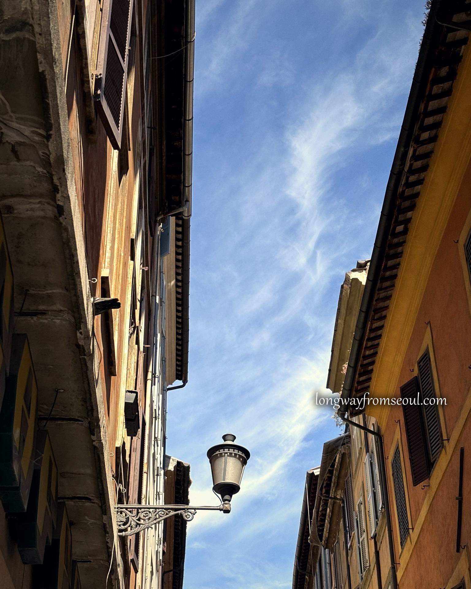 A wrought iron street lamp in a narrow Rome alley against blue sky