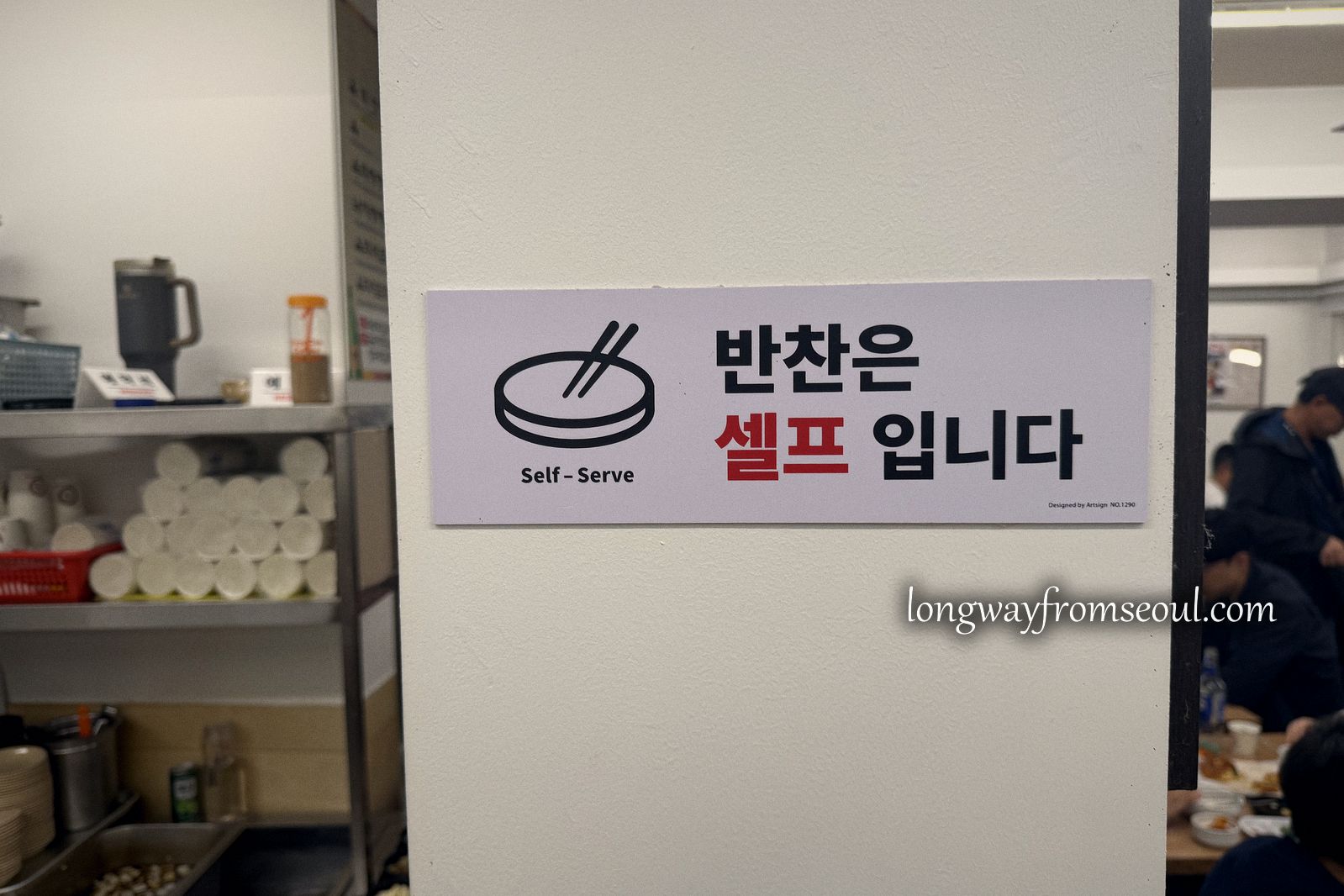 A sign inside a Gwangjang Market stall reading that side dishes are self-serve