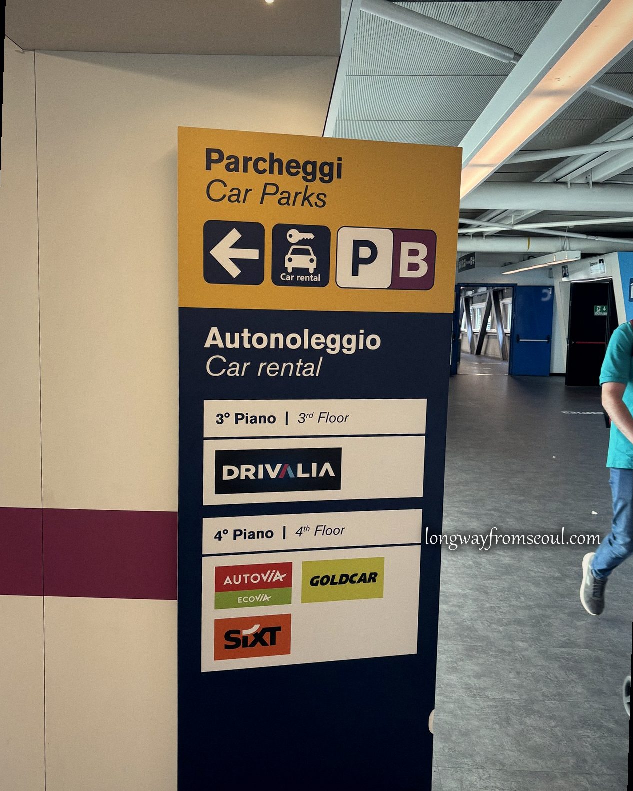 Car rental signage at Rome Fiumicino airport listing Drivalia, Autovia, Goldcar and Sixt