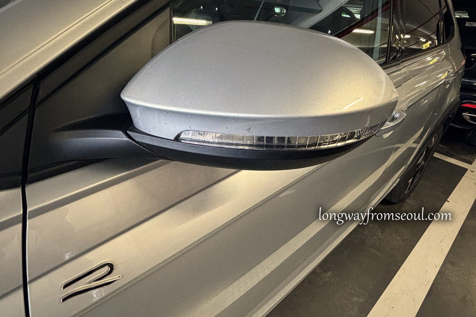 Close-up of a wing mirror on a silver rental car in an airport car park