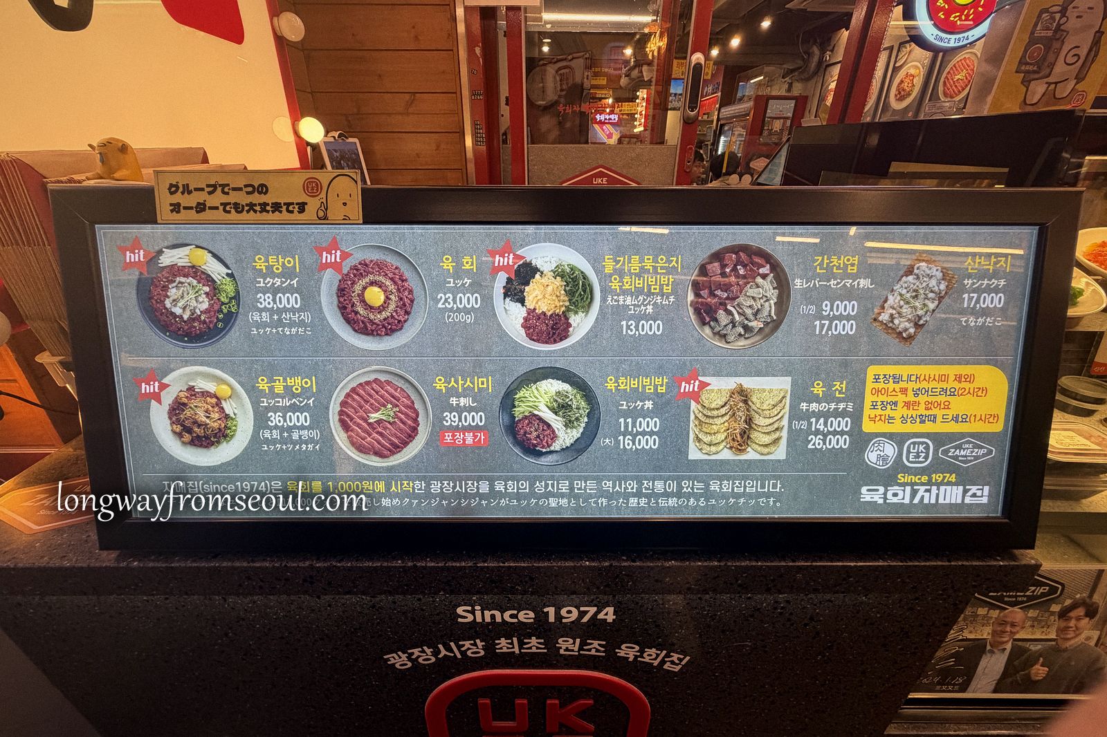 An illuminated menu board at Yukhoe Jamae-jip showing Korean raw beef dishes with prices