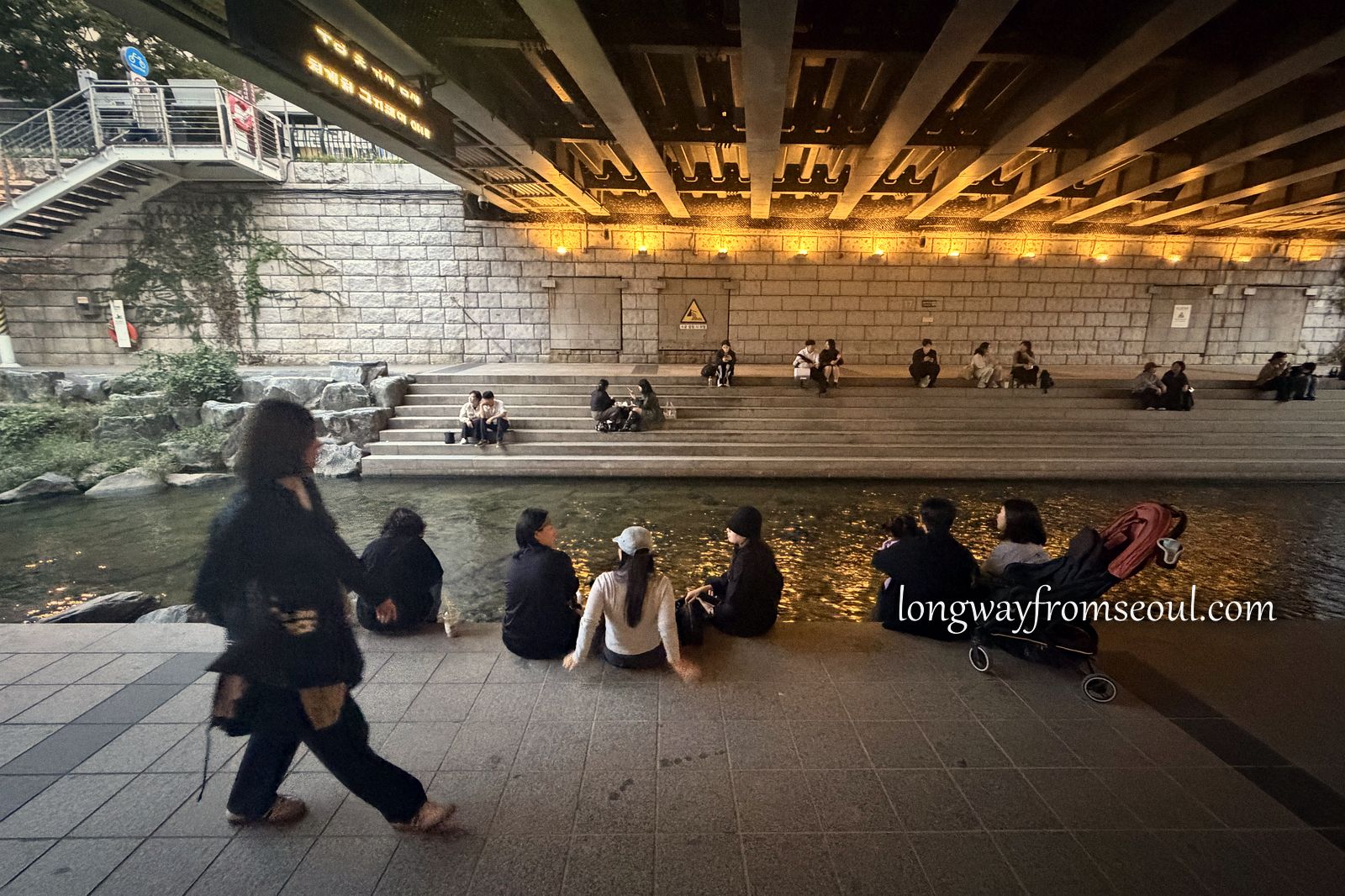 People sitting on stone steps along the Cheonggyecheon stream in central Seoul