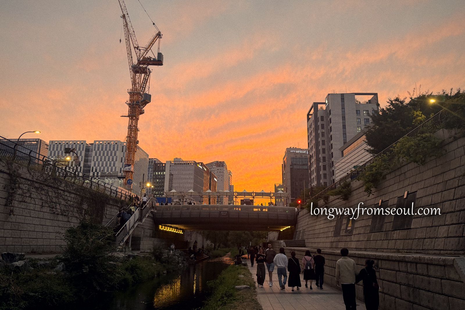 An orange sunset over the Cheonggyecheon stream and the buildings of central Seoul