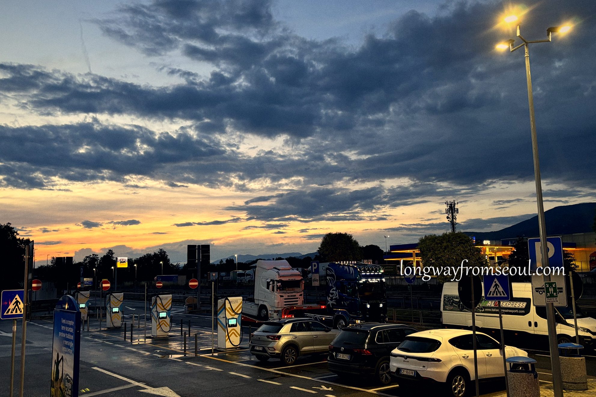 Cars and lorries at an Italian motorway service area in the last light