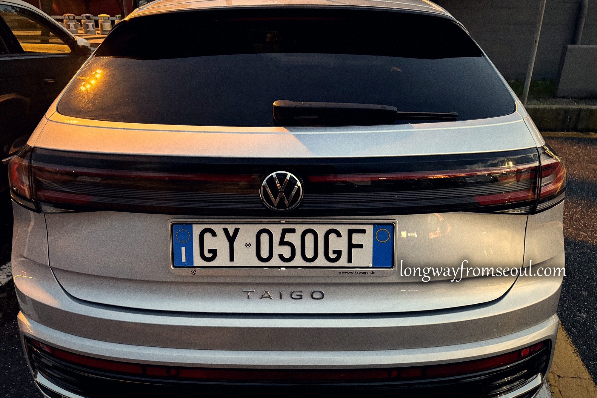 Rear of a silver Volkswagen Taigo rental car at dusk in a service station car park