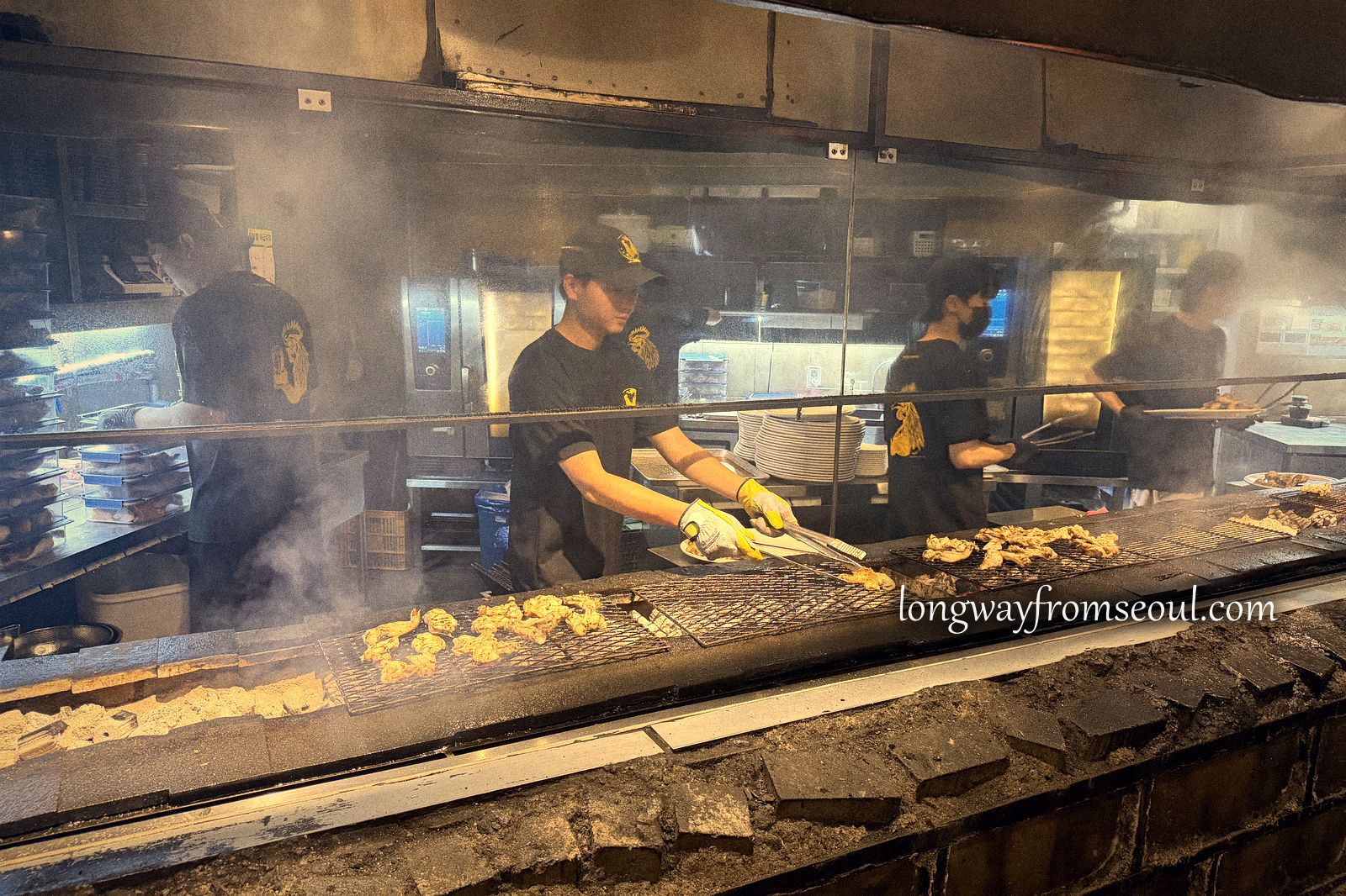 A long charcoal grill with meat cooking and smoke rising in an Euljiro street at night