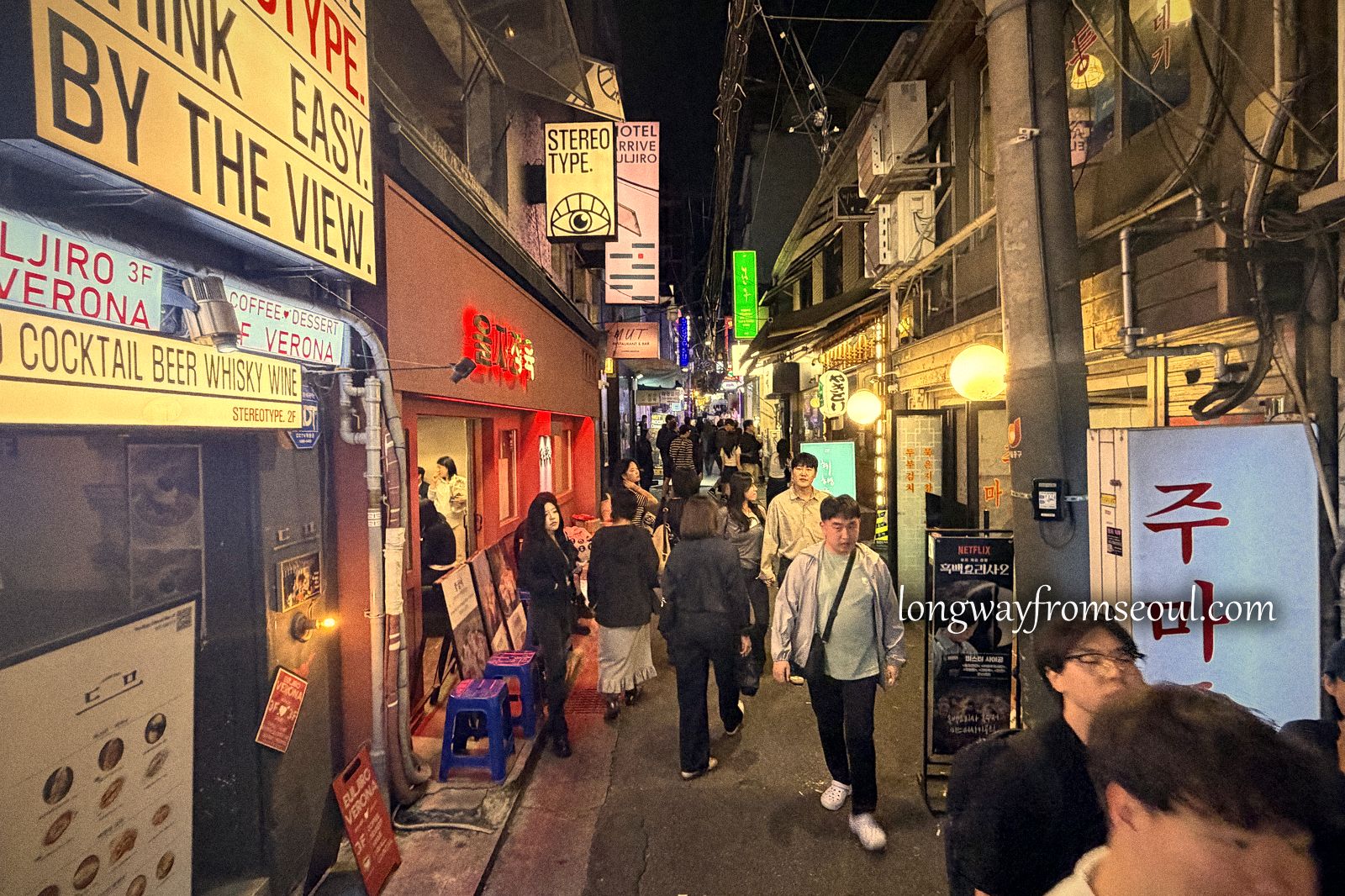 A bar street in Euljiro at night with illuminated signs and people walking