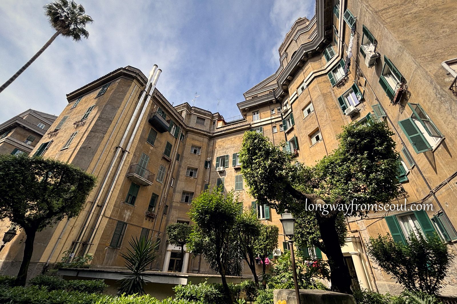 Looking up at the facade and palm trees of an apartment courtyard in Prati, Rome