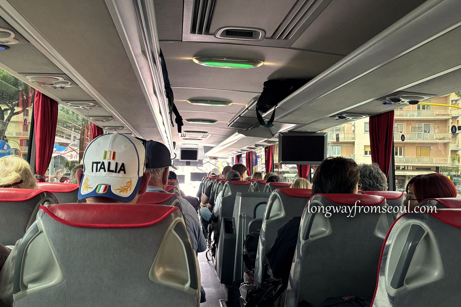 The interior of an airport shuttle coach in Rome with passengers and red seats